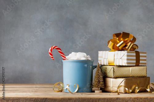 Winter lifestyle with cup of hot cocoa with marshmallows and Christmas gift or present boxes and holiday decorations on wooden background.
