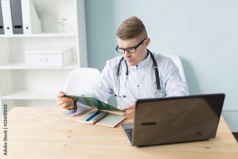 Medicine, working and people concept - handsome doctor sitting at the table and writing a recipe Medicine, working and people concept - handsome doctor sitting at the table and writing a recipe