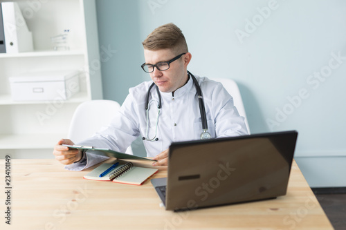 Medicine, working and people concept - handsome doctor sitting at the table and writing a recipe