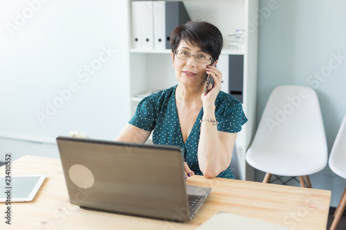 People, technology and communication concept - Adult business lady talking by phone in office