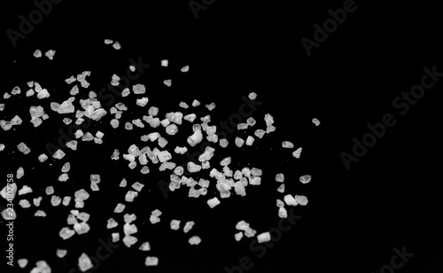 Spilled white sea salt on a black background. Transparent pebbles on a black background