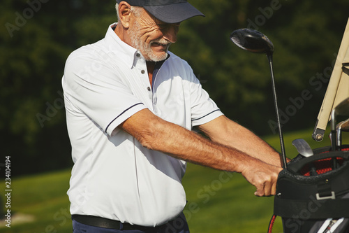 Senior man taking his club bag off a golf cart