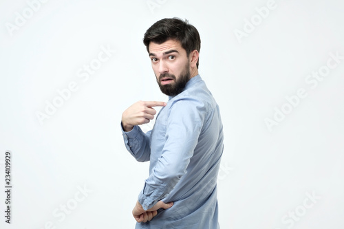 handsome frowning young hispanic man with voluminous hair pointing fingers at himself
