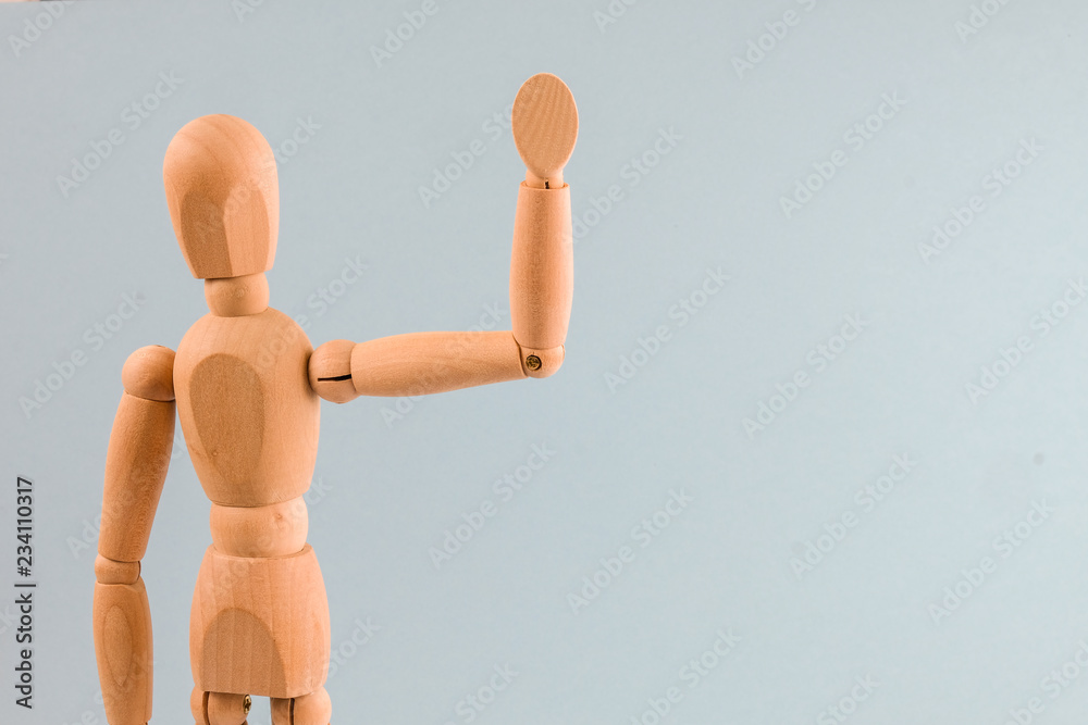 Wooden dummy waving hand on light blue background Wooden dummy waving hand on light blue background