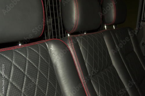 A view of a part of the interior of the car seat from leather of black color, stitched double thread of red color with contrast stitching in a vehicle interior design workshop