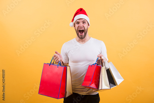 The morning before Xmas. delivery christmas gifts. man in santa hat hold christmas present. online christmas shopping. Happy new year. happy santa man on yellow background. Christmas fun. shoping bag