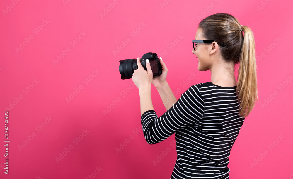 Young woman with a professional digital SLR camera on a pink background