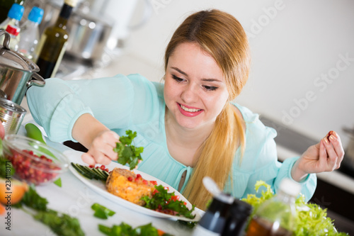 Young woman decorating salad with herbs in kitchen