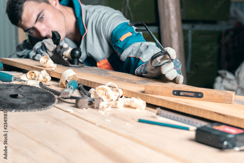 Man in overalls planing a tree in the Studio with a hand planer