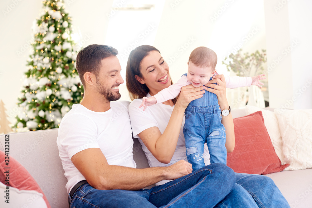 Happy young parents with their baby girl enjoy Christmas time while relaxing on the sofa. Family life. Happy young parents with their baby girl enjoy Christmas time while relaxing on the sofa. Family life.