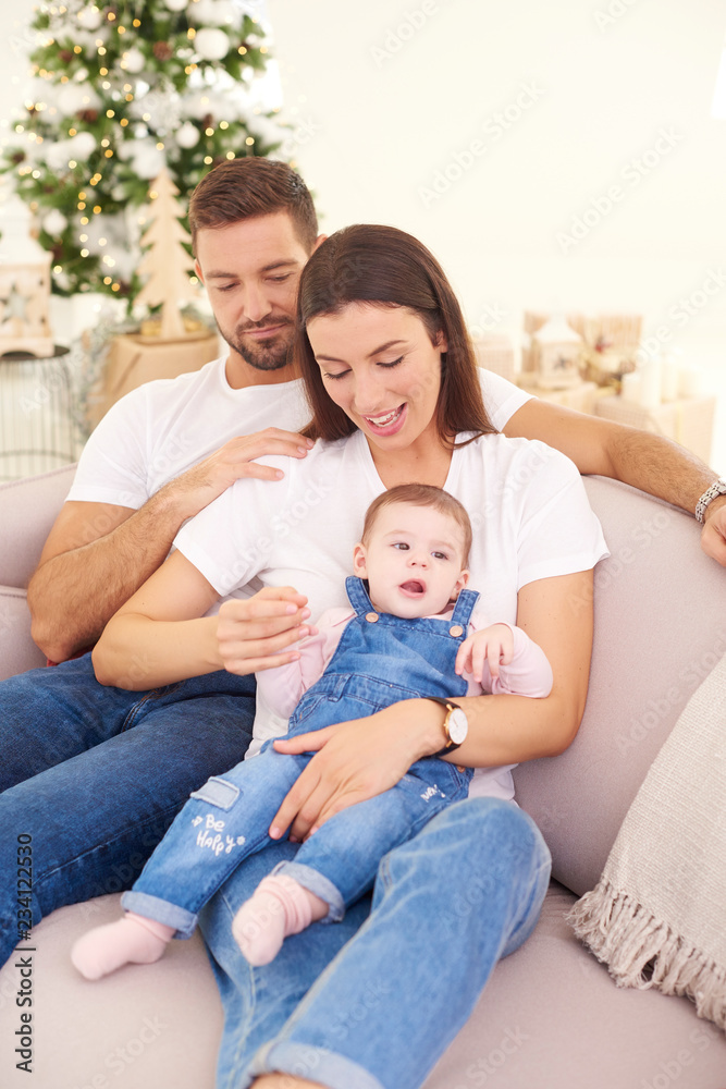 Happy young parents with their baby girl enjoy Christmas time while relaxing on the sofa. Family life. Happy young parents with their baby girl enjoy Christmas time while relaxing on the sofa. Family life.