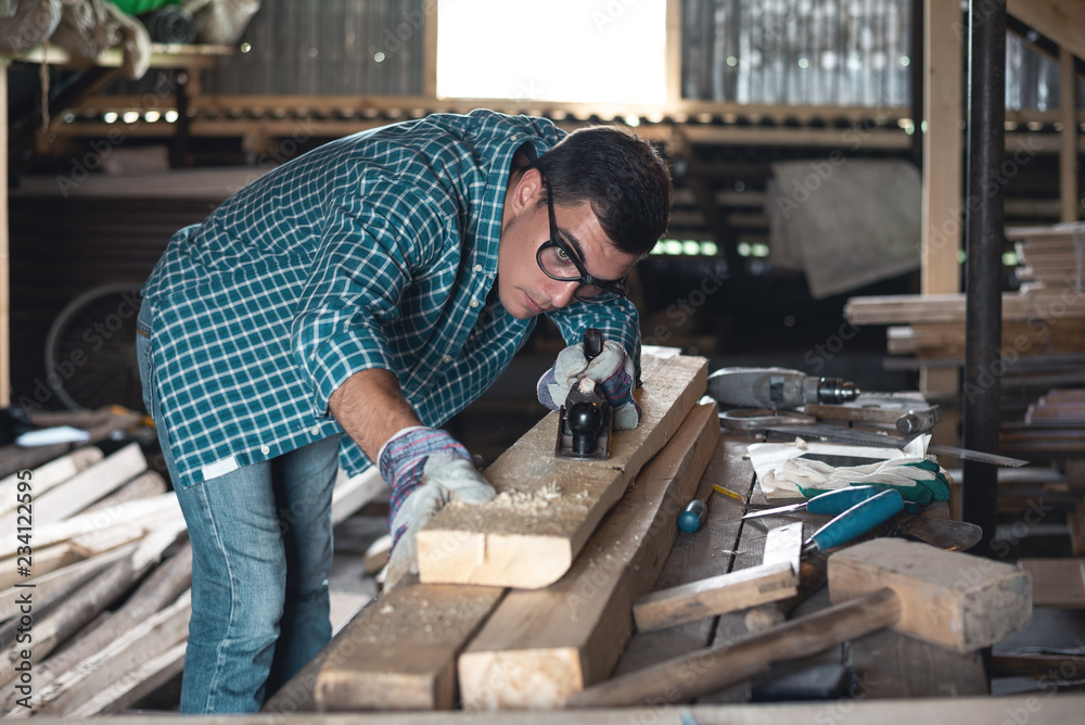 Man in a plaid shirt and jeans planing wood manual planer in the workshop Man in a plaid shirt and jeans planing wood manual planer in the workshop