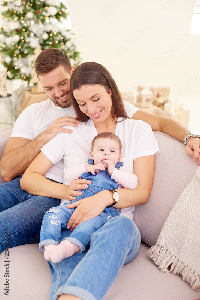 Happy young parents with their baby girl enjoy Christmas time while relaxing on the sofa. Family life. Happy young parents with their baby girl enjoy Christmas time while relaxing on the sofa. Family life.