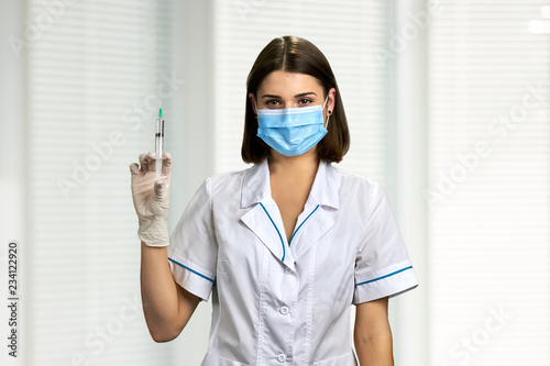 Female doctor in face mask holding syringe. Portrait of young woman doctor or nurse in protective gloves holding an injection.