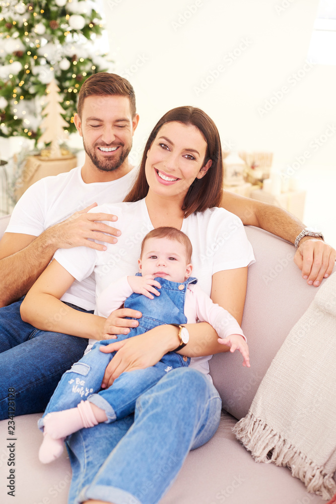 Happy young parents with their baby girl enjoy Christmas time while relaxing on the sofa. Family life. Happy young parents with their baby girl enjoy Christmas time while relaxing on the sofa. Family life.