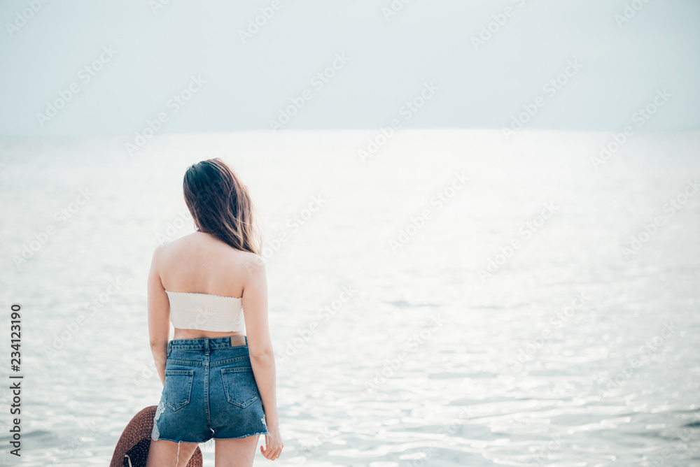 Woman in summer vacation wearing straw hat and beach dress enjoying the view at the ocean Woman in summer vacation wearing straw hat and beach dress enjoying the view at the ocean