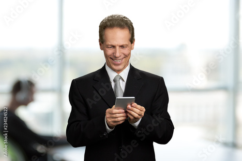Happy businessman looking at his smartphone. Handsome mature man in business suit reading a message on his smartphone and smiling.