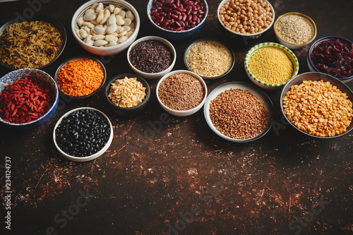 Various superfoods in smal bowls on dark rusty background. Superfood as rice, lentil, beans, peas, goji, flaxseed, buckwheat, couscous, chickpeas Copy space for text