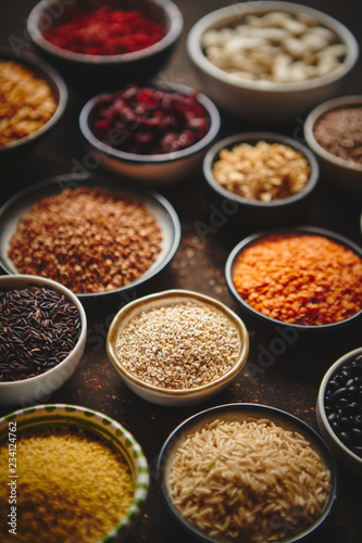 Various superfoods in smal bowls on dark rusty background. Superfood as rice, lentil, beans, peas, goji, flaxseed, buckwheat, couscous, chickpeas Above view Flat lay