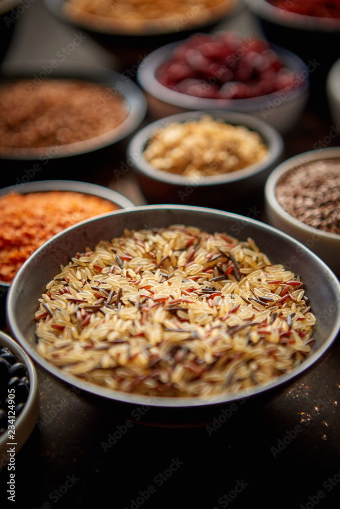 Raw wild rice in ceramic bowl. Composition of superfoods in background. Placed on dark rusty table. Selective focus. Raw wild rice in ceramic bowl. Composition of superfoods in background. Placed on dark rusty table. Selective focus.