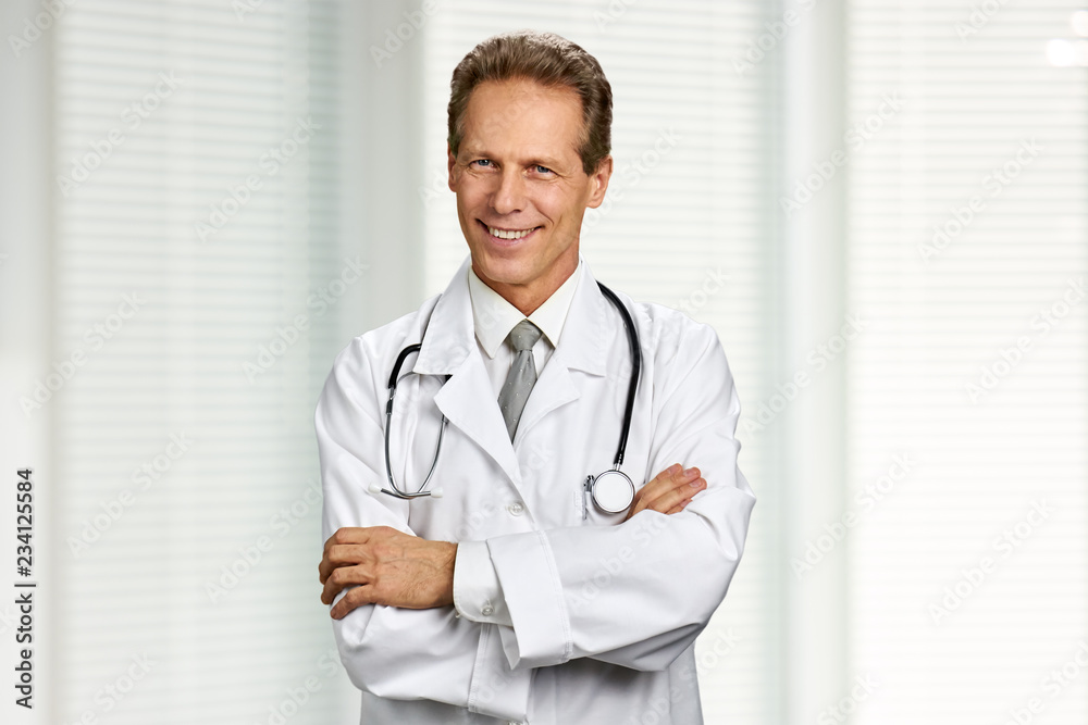 Portrait of cheerful doctor with crossed arms. Smiling male doctor with stethoscope folded arms on blurred background. People, occupation, healthcare. Portrait of cheerful doctor with crossed arms. Smiling male doctor with stethoscope folded arms on blurred background. People, occupation, healthcare.