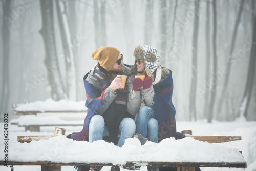 Young couple with blanket drinking coffee outdoors in snow