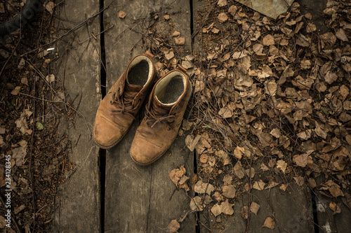 A pair of nubuck hiking boots on wooden floor with dead leaves ang twigs. Top view, empty space photo