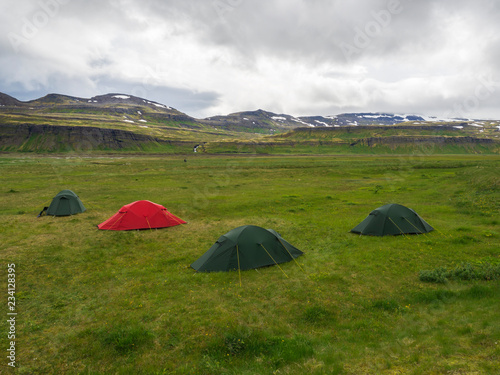 Hornvik campsite with three green tents and one red and view on beautiful Hornbjarg cliffs in remote nature reserve with green meadow, waterfall and hills, moody sky, Iceland, west fjords Hornstrandir photo