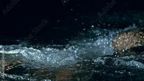 Slow motion of waves on dark water surface with play of flecks of bright light close up. Amazing dramatic natural background. Shooting with 180fps. Epic mystical and magic night view. Crystal clear photo
