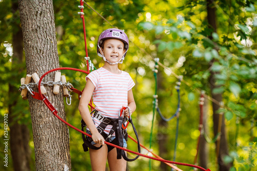 girl with climbing gear in an adventure park are engaged in rock climbing or pass obstacles on the rope road.