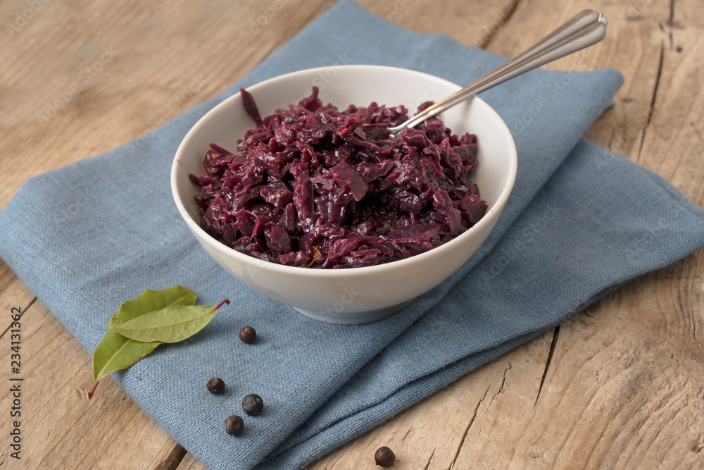 cooked red cabbage in a bowl, juniper berries and bay leaf on a blue napkin on a rustic wooden table, copy space cooked red cabbage in a bowl, juniper berries and bay leaf on a blue napkin on a rustic wooden table, copy space