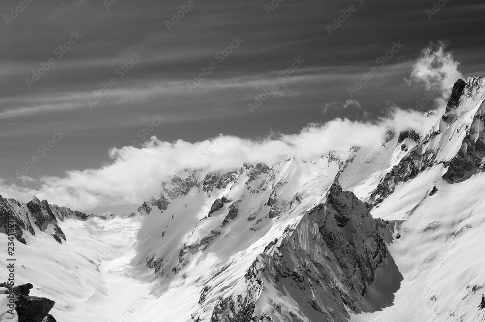 Black and white snowy mountains in clouds at sun wind day