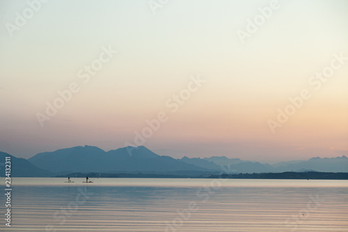 A couple practicing paddlesurf at sunset on a lake