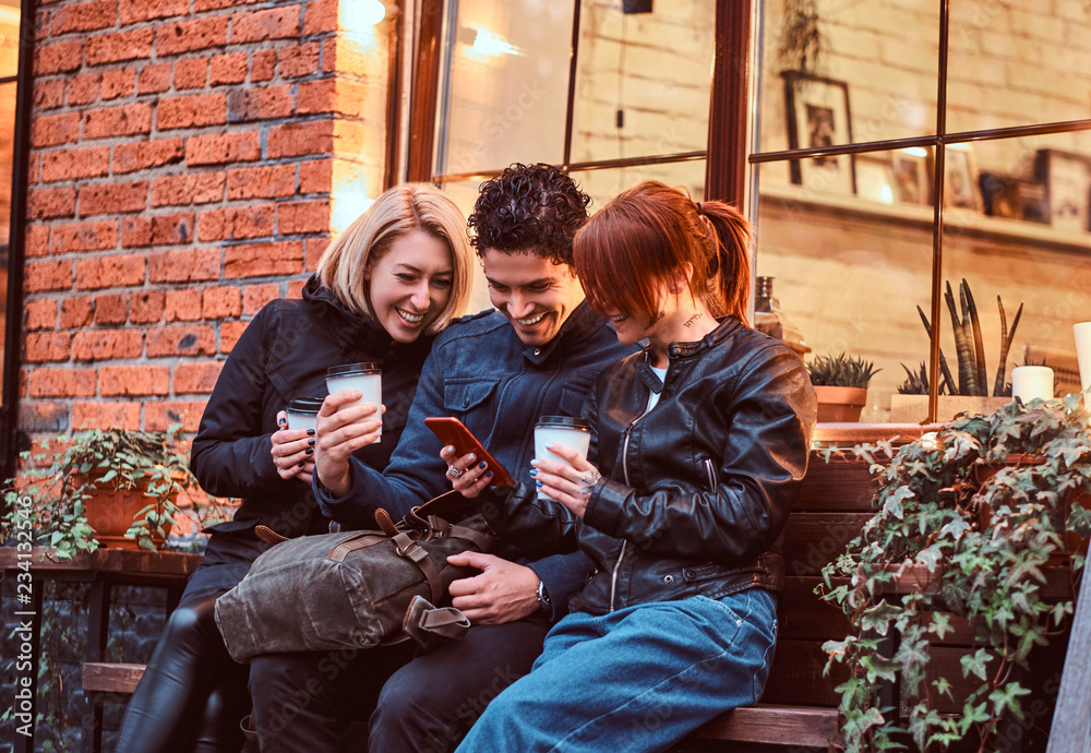 Three happy friends having a break with coffee sitting near a cafe outside. Three happy friends having a break with coffee sitting near a cafe outside.