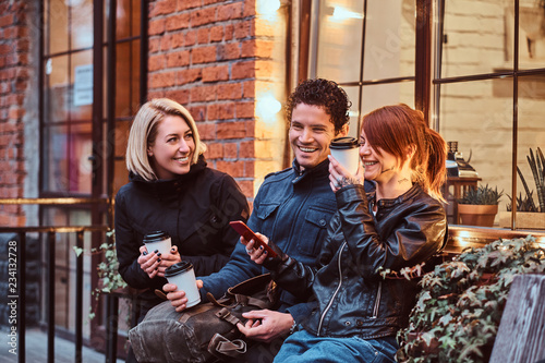 Three happy friends having a break with coffee sitting near a cafe outside.