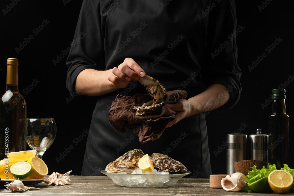 The chef opens an oyster on a background of white wine, lettuce, lemons and limes