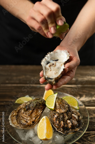 oysters in a plate with ice and lemon, in the hands of the chef pour lime on a wooden background. Seafood, restaurant, delicious taste