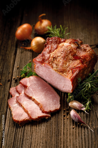 Smoked meats, sliced smoked pork loin on a wooden  table with addition of fresh  herbs and aromatic spices.  