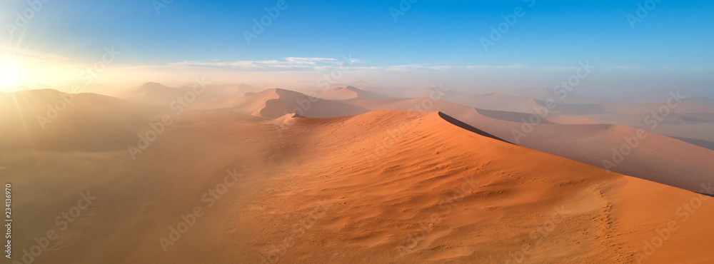 Panoramic, aerial, artistic photo of Namib dunes.  Early morning Namib desert covered in mist. Orange dunes of Namib from above. Desert landscape. Sunrise in Namib-Naukluft  desert. Traveling Namibia. - obrazy, fototapety, plakaty 