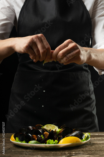 Chef pouring lemon juice with mussels with white wine salad on a dark background