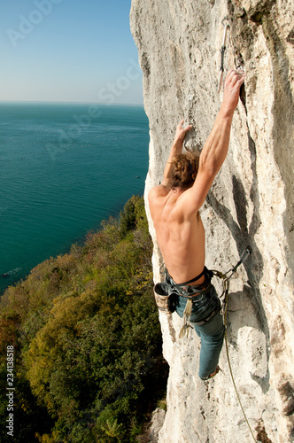 Young athletic man training rock climbing in front of the sea in Trieste, Italy . Vertical frame sunny day.