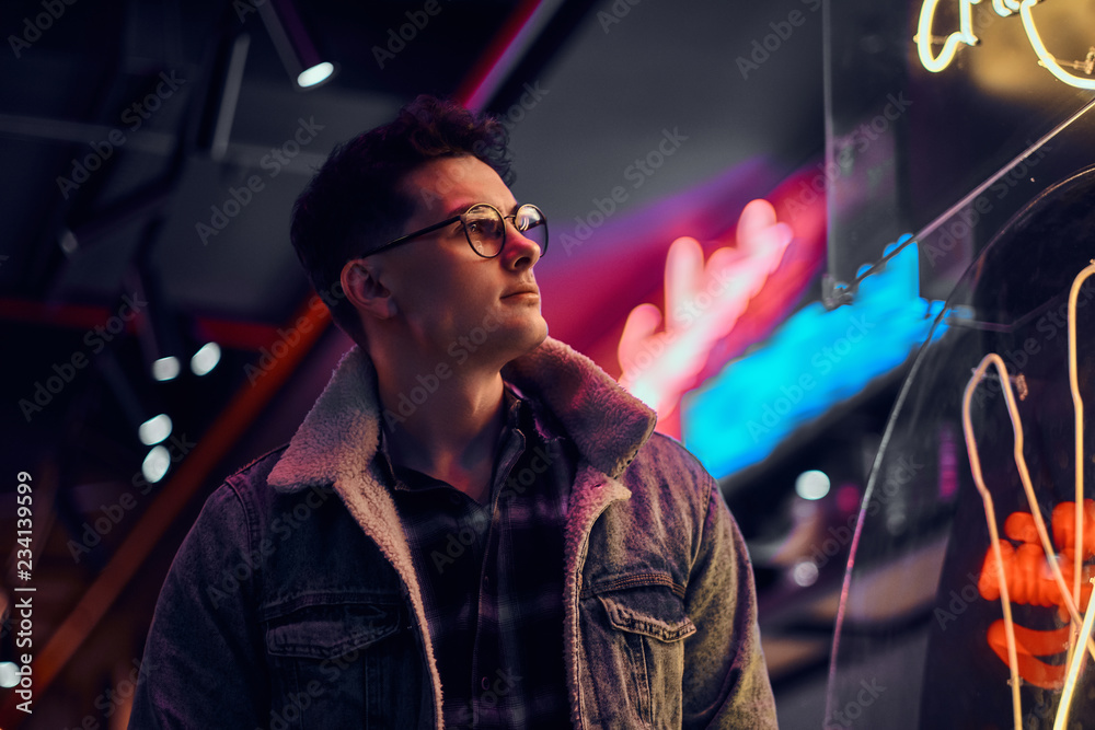A young man fashionably dressed standing in the street at night. Illuminated signboards, neon, lights. A young man fashionably dressed standing in the street at night. Illuminated signboards, neon, lights.