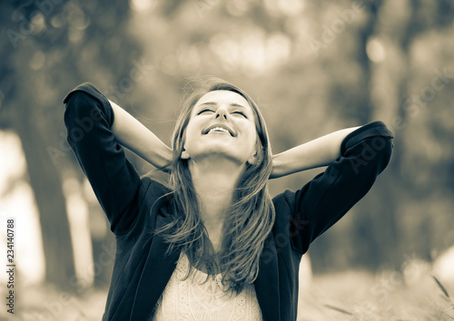 Beautiful girl in jacket sitting on grass in a park. Image in sepia color style