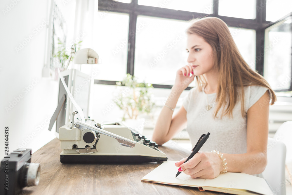Young business woman working at home behind a typewriter and writes in a diary. Creative Scandinavian style workspace Young business woman working at home behind a typewriter and writes in a diary. Creative Scandinavian style workspace