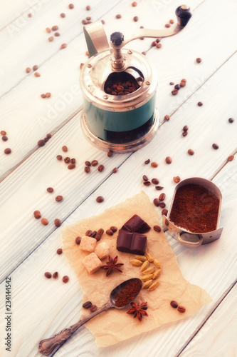 Close-up shot of vintage hand-operated old coffee grinder, roasted beans, chocolate, badyan and cardamom on a rustic wooden table. photo