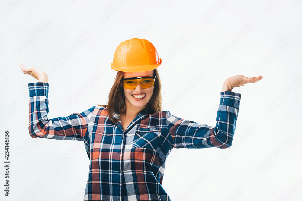 Happy young girl in blue and red shirt, glasses and orange protective helmet. Beautiful smiling woman in building helmet showing balance with her hands on white background. Happy young girl in blue and red shirt, glasses and orange protective helmet. Beautiful smiling woman in building helmet showing balance with her hands on white background.