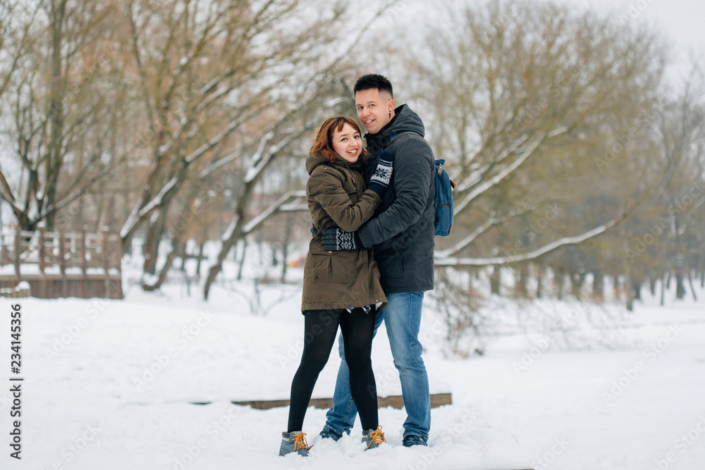 Winter portrait of young beautiful happy smiling couple outdoors. Christmas and winter holidays. Man and woman in snowy park