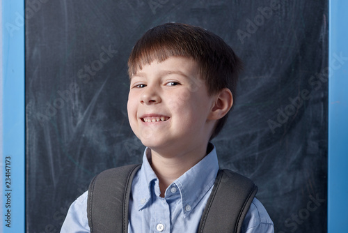 Smiling clever boy with backpack against blackboard. © Artem
