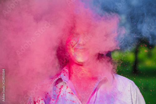 Closeup portrait of emotional woman posing in a cloud of pink and blue Holi paint in the park