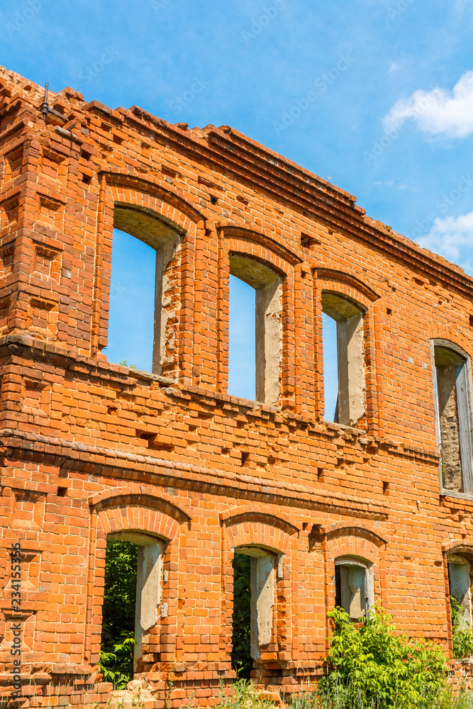 A large ruined ancient house of red brick against a blue sky with white clouds.